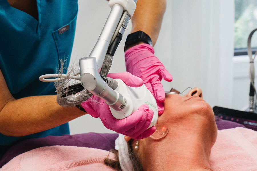 Licensed aesthetic provider performing a laser skin resurfacing treatment on a patient's face using advanced laser technology in a modern medical spa.